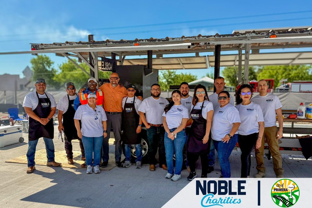 Volunteers in Noble Charities shirts and aprons standing at the smoker trailer at the Primera flood relief BBQ